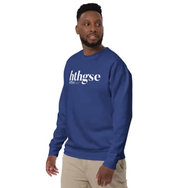 A man wearing a royal blue Unisex Crew Neck Sweatshirt with the white text hthgse stands sideways, his head turned as he looks off to the side. He pairs it with khaki pants against a plain white background.