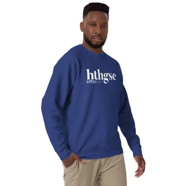 A man wearing a blue unisex crew neck sweatshirt with a white logo and the text hthgse and F I T H stands facing the camera, one hand at his side and the other slightly raised. He is also wearing light-colored pants.