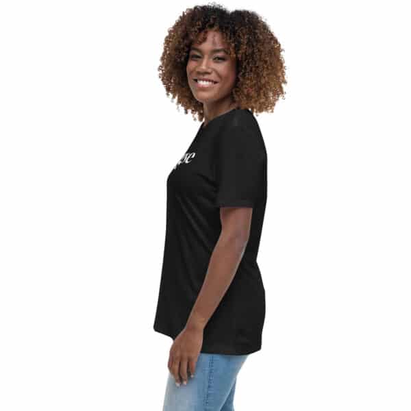 A woman with curly hair, wearing a Women's Relaxed Fit T-Shirt in black and blue jeans, stands smiling and facing sideways against a plain white background.