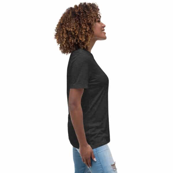 A woman with curly hair smiles and stands in profile, wearing a dark gray Women's Relaxed Fit T-Shirt and light ripped jeans, against a plain white background.