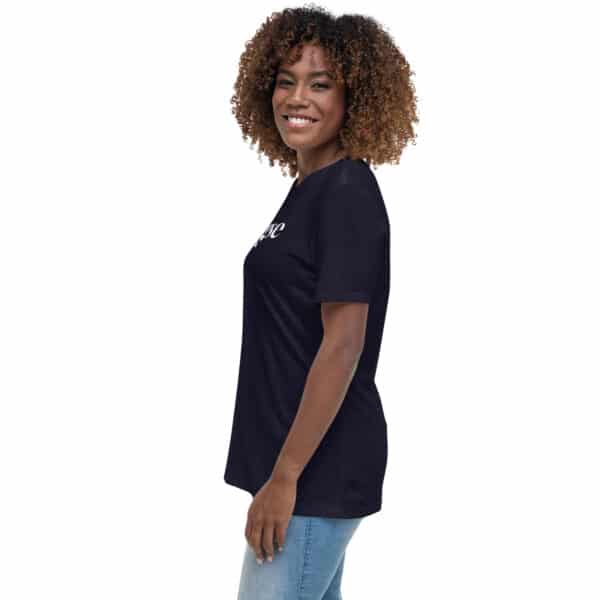 A woman with curly hair smiles while standing sideways, wearing a Women's Relaxed Fit T-Shirt with a white logo and light blue jeans against a white background.