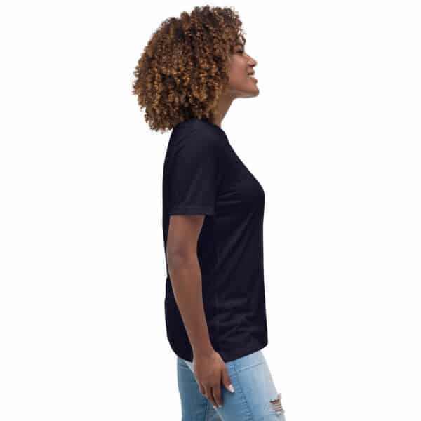A woman with curly hair stands in profile, smiling and wearing a black Women's Relaxed Fit T-Shirt and light blue ripped jeans, set against a plain white background.