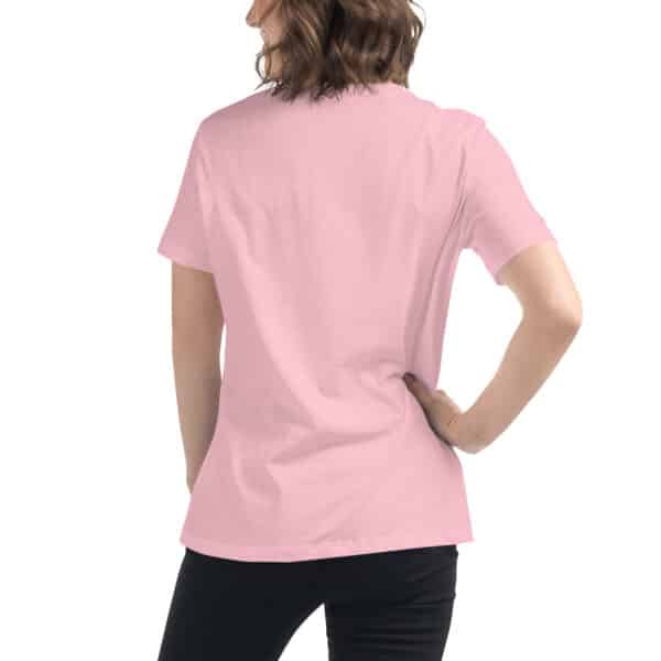 A person with wavy, shoulder-length brown hair stands with their back to the camera, wearing a plain Women's Relaxed Fit T-Shirt in pink and black pants, with one hand resting on their hip.