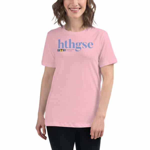 A smiling person wears a light pink Women's Relaxed Fit T-Shirt with "hthgse" in large blue letters and a small full color logo and text beneath it, standing against a white background.
