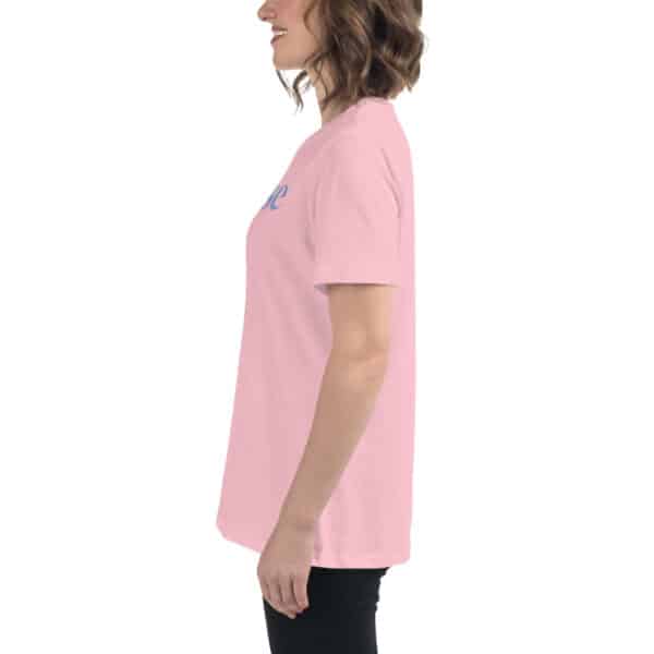 A woman stands in profile, smiling, wearing a light pink Women's Relaxed Fit T-Shirt and black pants against a white background.