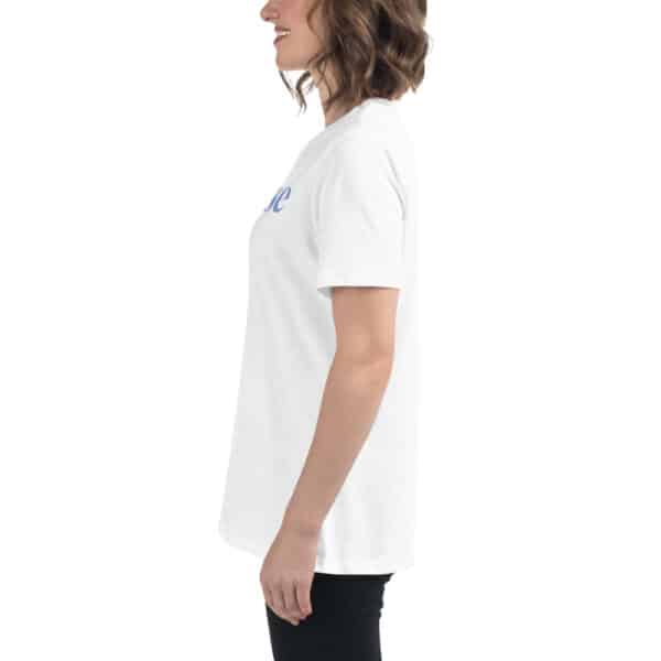 A woman with wavy brown hair, wearing a Women’s Relaxed Fit T-Shirt and black pants, stands in profile facing left and smiling against a plain white background.