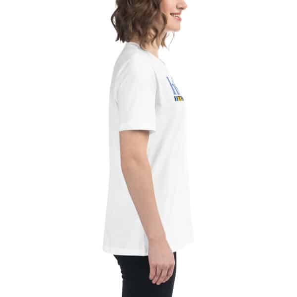 A woman with wavy brown hair wearing a Women's Relaxed Fit T-Shirt and black pants stands in profile, smiling, against a plain white background.