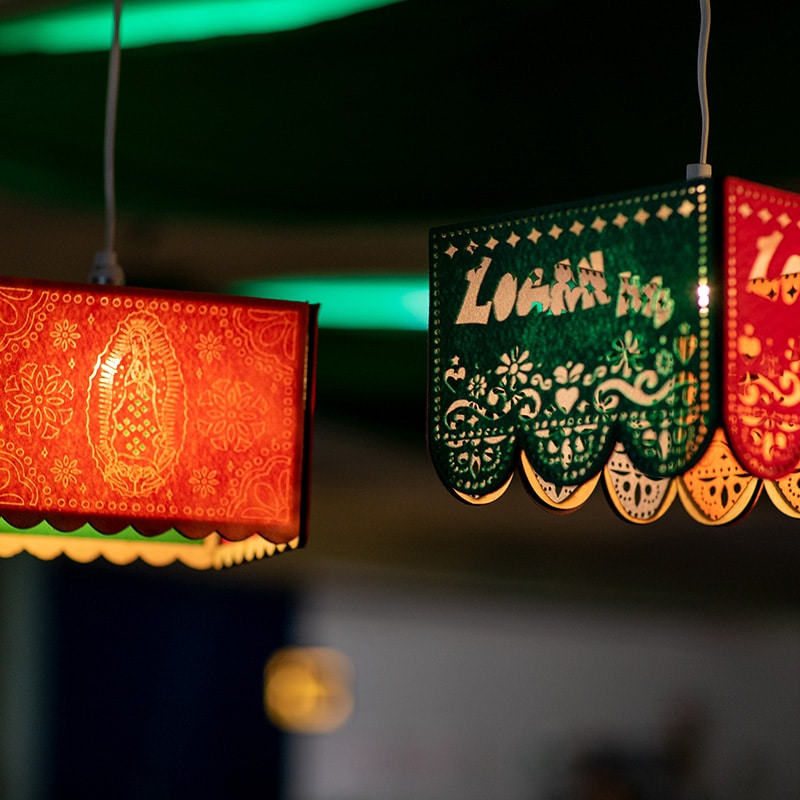 Two colorful, rectangular hanging lanterns with intricate cutout patterns, one red and one green, illuminated from within—perfect for inspiring model critiques or enhancing any instructional practice setting. The green lantern features scalloped edges and partial white text.