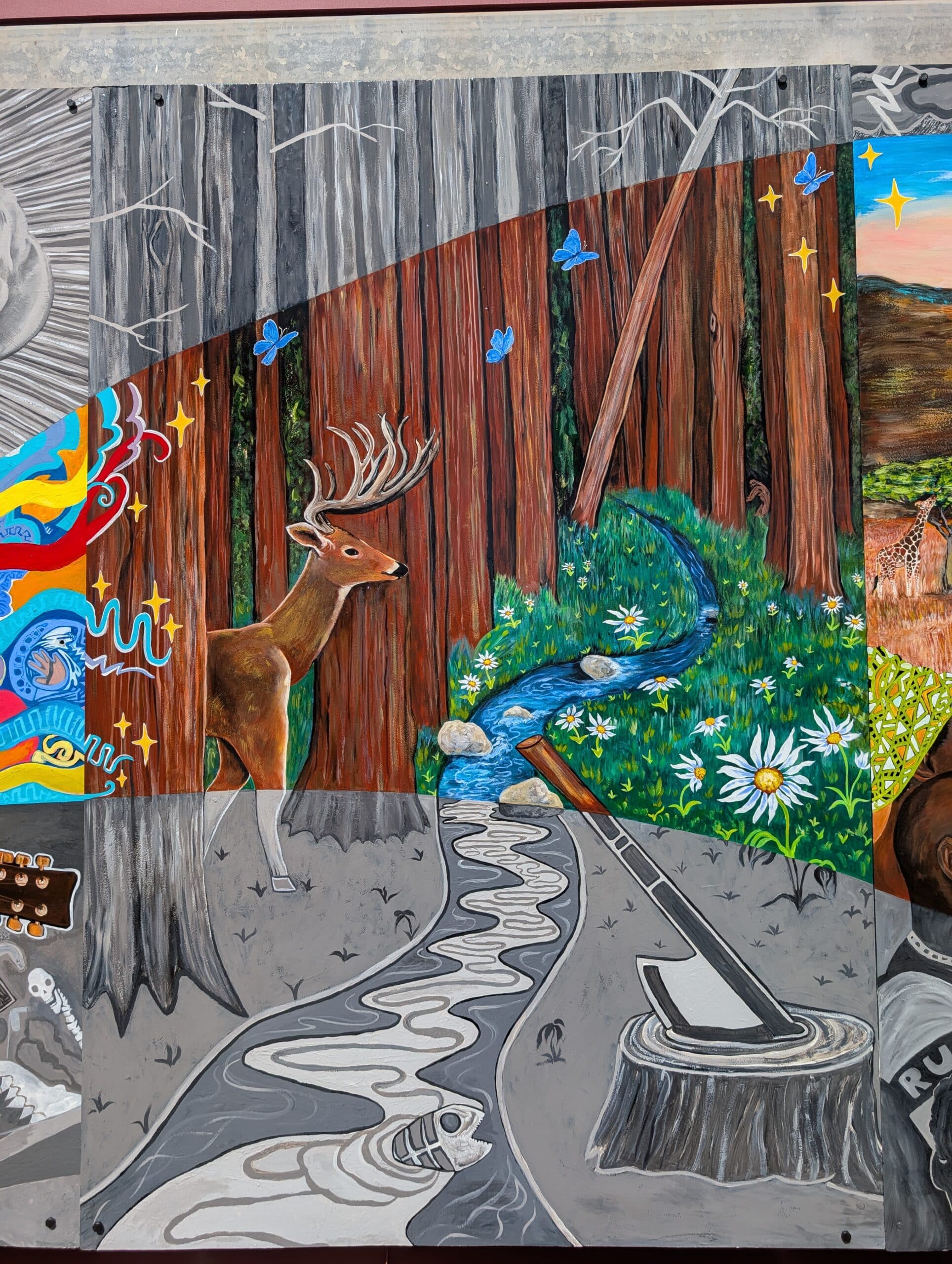 A mural section from the Imagine Mural Project depicts a vibrant forest with a deer, blue butterflies, daisies, and a stream—contrasting with a grayscale area below that honors a life, showing an axe over a log beside a winding river.