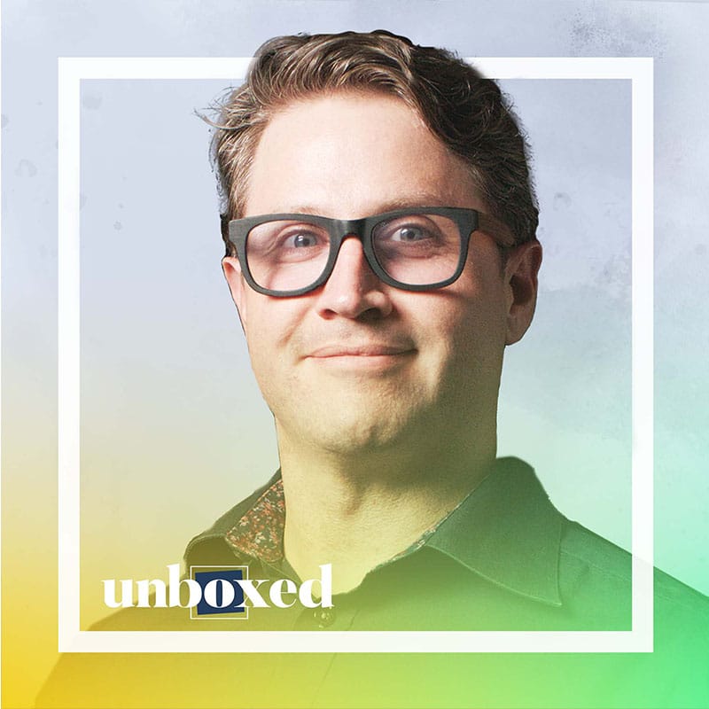 A man with light brown hair and glasses smiles softly, wearing a dark collared shirt. The image has a white square frame and a soft gradient overlay with the word unboxed at the bottom, created to honor a life as part of the Imagine Mural project.