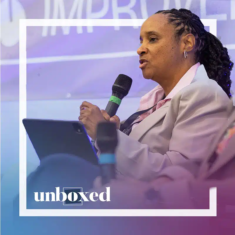 A woman in a light suit speaks into a microphone while holding a tablet, seated in a panel discussion setting. “Unboxed” and “Mississippi Miracle” appear at the bottom with a blue and purple gradient overlay.
