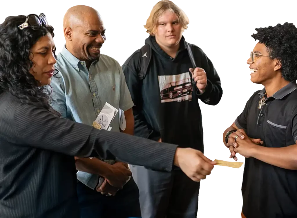 Four people stand together, smiling and talking. One person is handing something, possibly a card or paper, to another while the others look on. One person wears a backpack. The background is plain white.